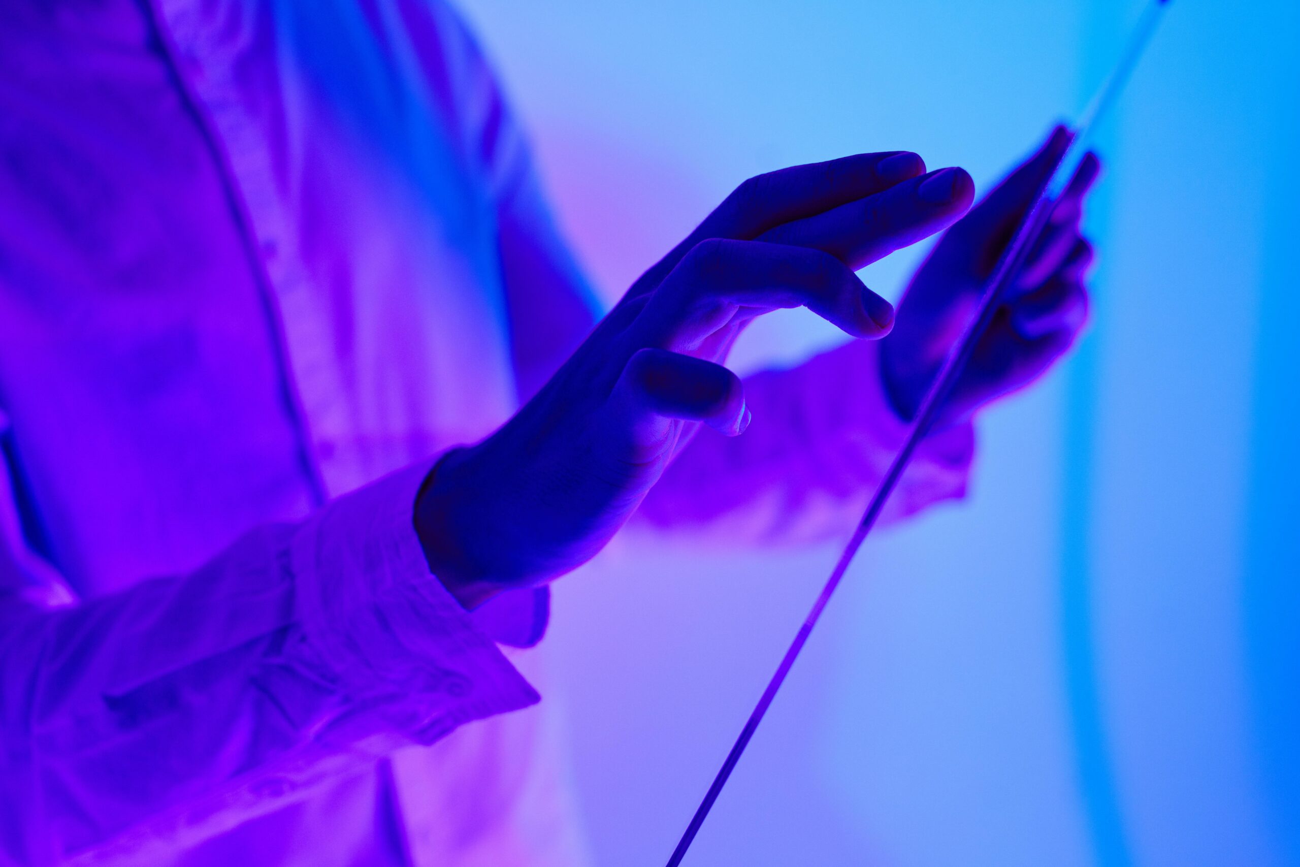 Close-up of hands interacting with a futuristic holographic glass interface in vibrant purple and blue lighting.